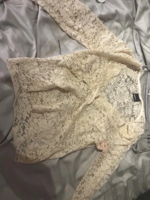 Krämvit spetsblus med lång ärm - Säljer en krämvit blus i genombruten spets med långa ärmar. Blusen har ett romantiskt blommönster och är lätt transparent, perfekt för lager på lager. Modellen är figurnära och ger en elegant look.