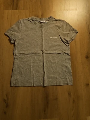 Grå t-shirt från Borg - En stilren grå t-shirt från Borg med enkel design och rund hals. T-shirten har korta ärmar och en liten vit logga på bröstet. Perfekt för en avslappnad och sportig look.