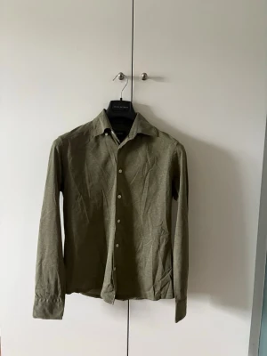 Grön Eton skjorta - Grön Eton skjorta i storleken S slim fit. Skjortan är i mycket bra skick, och stryker självklart den innan frakt! Säljes då den är för liten.