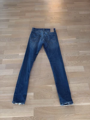 Blå replay jeans - Säljer ett par klassiska replay jeans i mörkblå tvätt med slitningar och råa, fransiga benslut. Jeansen har fem fickor, normal passform och är tillverkade i bomull med en smal siluett. Perfekta för en avslappnad och trendig look.