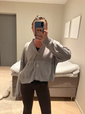 Ljusgrå oversized kofta med stora knappar - Säljer en ljusgrå oversized kofta med stora, runda knappar framtill och två fickor. Koftan har en avslappnad passform och ribbade muddar vid ärmslut och nederkant. Perfekt för lager-på-lager och chill vardagsstil.