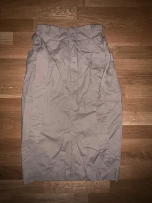 Beige cargokjol med fickor - Säljer en beige cargokjol med hög midja och stora sidofickor. Kjolen har en rak passform och är tillverkad i ett slitstarkt bomullsmaterial. Perfekt för dig som gillar utility-stilen och vill ha något både snyggt och praktiskt.