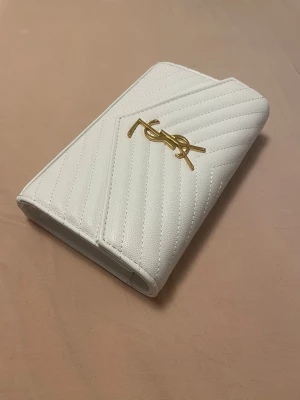Vit quiltad axelväska från YSL - Kvitto finns, pris kan diskuteras! Säljer en snygg vit axelväska från YSL med guldfärgad kedja och ikonisk YSL-logga framtill. Väskan är quiltad i ett elegant mönster och har en stilren, strukturerad form. Perfekt för dig som vill ha en lyxig accessoar med exklusiv känsla.