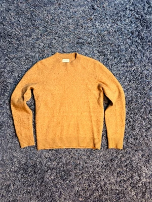 Brun stickad tröja - Mysig brun stickad tröja med rund hals och ribbade muddar vid ärmslut och nederkant. Tillverkad i en mjuk ullmix som håller dig varm under kyliga dagar. Enkel och stilren design som passar till det mesta. Den är lite nopprig men går såklart att noppra av, hör av er vid minsta fundering!