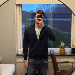 Mörkblå kofta Sand Copenhagen - Snygg mörkblå kofta från Sand Copenhagen med dragkedja framtill och diskreta ribbade detaljer över bröstet och axlarna. Riktigt skönt material och perfekt för lager på lager. Står ingen storlek på den men sitter bra på mig som är 180, ca 70kg (Skulle säga runt S-M hållet). Hör av vid funderingar!