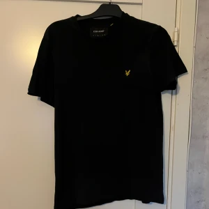Svart t-shirt från Lyle & Scott - Svart t-shirt från Lyle & Scott i storlek M. Klassisk design med rund hals och korta ärmar. På bröstet finns den ikoniska gula fågeln som broderad detalj. T-shirten är gjord i mjuk bomull. Den är i superfint skick och har ej använts så himla mycket. Hör av er om ni har frågor!