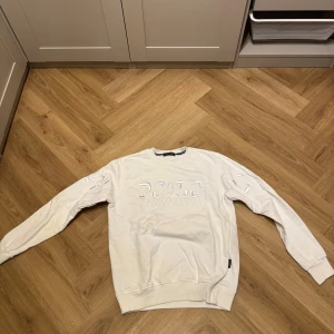 Vit sweatshirt från Polo Ralph Lauren - Säljer en vit sweatshirt från Polo Ralph Lauren med broderad logga och detaljer på bröstet och ärmarna. Tröjan har rund hals, långa ärmar och ribbade muddar. Perfekt för dig som gillar klassisk och stilren streetwear.