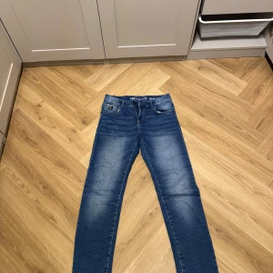 Blå jeans från LAB Industries, storlek 164 - Snygga blå jeans från LAB Industries i storlek 164. Klassisk femficksmodell med ljusa slitningar framtill och bak, raka ben och normal passform. Jeansen är tillverkade i hållbar denim och har en cool tvättad look som passar perfekt till streetwear.