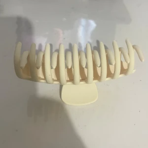 Beige hårklämma i matt plast - Stilren beige hårklämma med matt finish och breda, rundade taggar. Perfekt för att snabbt sätta upp håret i en snygg och enkel look. Klämman är tillverkad i tålig plast och har en modern, minimalistisk design.