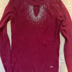 Vinröd stickad tröja med pärlor från Mitsy - Supersnygg vinröd stickad tröja från Mitsy med lång ärm och ett coolt nyckelhålsutskärning vid halsen. Dekorerad med pärlor i ett mönster som ger extra bling. Perfekt för dig som gillar detaljer och vill sticka ut lite extra. Snabb leverans 📦kolla görna på mina andra plagg