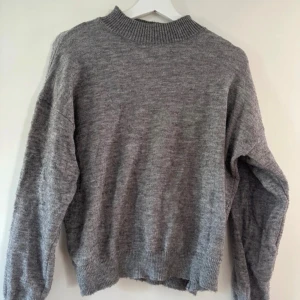 Grå stickad tröja från Shein - Mysig grå stickad tröja från Shein i storlek S. Tröjan har en ribbad hög hals och långa ärmar med ribbade muddar. Perfekt för kyliga dagar och enkel att matcha med jeans eller kjol. 