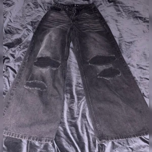 Gråa wide-leg jeans med slitningar slit jeans EU 34 / XS - Gråa wide leg jeans från Missguided med stora slitningar över knäna. Hög midja och fickor. Jeansen är i denim och har dragkedja framtill.