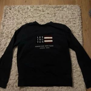 Blå sweatshirt från Lexington - Säljer en svart sweatshirt från Lexington med broderad logga och text framtill. Tröjan har långa ärmar och klassisk passform, perfekt för en avslappnad stil. Mjukt bomullsmaterial som är skönt mot huden.