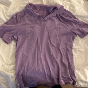 Ljuslila kortärmad pikétröja H&M - Snygg ljuslila pikétröja med klassisk krage och korta ärmar. Tröjan är tillverkad i mjukt bomullsmaterial och har en enkel, stilren design utan mönster eller detaljer. Perfekt för dig som gillar färg och vill ha en chill look.