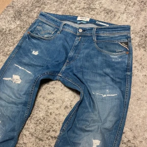 Replay Anbass blå jeans med slitningar - Feta replay jeans med slitningar. Säljes pga används inte längre. 10/10 skick använda fåtal ggr. Obs original storleken är 32/34 men har kortat ned benen så sitter som 32/32