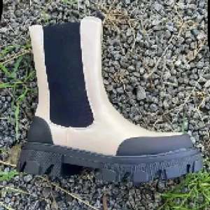 Beige chunky chelsea boots 38 NYA - Snygga beige chelsea boots med svarta elastiska paneler och grov, svart platt sula. Bootsens ovandel är i skinnimitation och har svarta detaljer vid tå och häl. Perfekt för dig som gillar trendiga och robusta skor med cool kontrast.