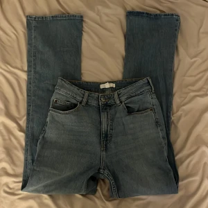 Blå jeans  - Säljer ett par klassiska blå jeans med raka ben och hög midja. Färgen är en snygg mellanblå tvätt. Har en liten fläck på benet.