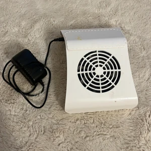 Elektrisk dammsugare för naglar - Elektrisk dammsugare för naglar med medföljande strömadapter. Vit plastkropp med synliga fläckar och mindre slitage. Utrustad med filter för effektiv uppsamling av nageldamm. Perfekt för manikyr och salongsbruk.