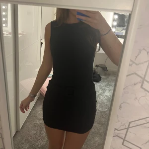 Svart ärmlös miniklänning med bälte - Snygg svart ärmlös miniklänning med rund hals och ett matchande bälte i midjan. Klänningen har en tight passform och är perfekt för dig som gillar en stilren och enkel look. Passar dig som vill ha en klassisk svart klänning med modern touch. Aldrig använd men är utan prislapp💕