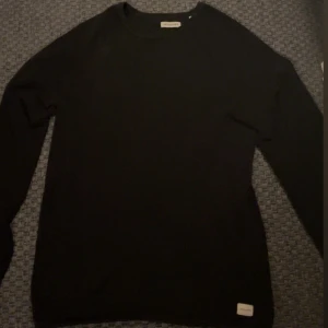 Svart stickad tröja Jack & Jones - En svart stickad tröja från Jack & Jones med rund halsringning och diskret logotyp-patch nertill. Tröjan har lång ärm och en klassisk, enkel design som funkar till allt. Perfekt för dig som gillar stilrena och bekväma plagg.