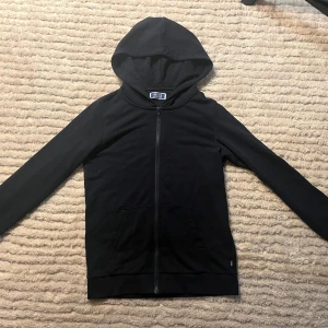 Mörkblå hoodie från Jack & Jones - Mörkblå hoodie från Jack & Jones med dragkedja framtill och huva. Tröjan har långa ärmar, två fickor fram och en clean, enkel design. Perfekt för dig som gillar en stilren look och vill ha något bekvämt till vardags.