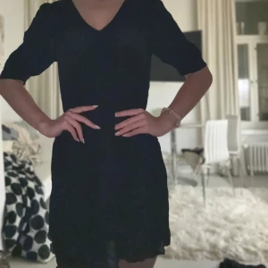 Svart kort klänning från Vero Moda - Supersnygg svart kort klänning från Vero Moda med v-ringning och puffiga halvlånga ärmar. Klänningen har smock i midjan för en smickrande passform och är gjord i ett lätt, flowy material som känns skönt mot huden.