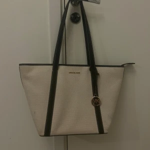 Beige axelväska från Michael Kors - Jag säljer denna super fina äkta Michael Kors väska i ett jättebra skick. Väskan säljs med original påse och kvitto. Den ända defekten är två små fläckar (se bild 1) men de går troligen väldigt enkelt att få bort. Kan gå ner i pris vid snabb affär❤️❤️