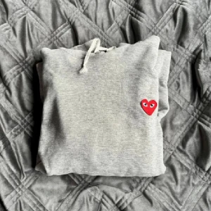 Grå hoodie Comme des Garçons Play - Grå hoodie från Comme des Garçons. Enda defekten är ett litet hål vid armbågen, fråga gärna om bild på det om ni är intresserade!