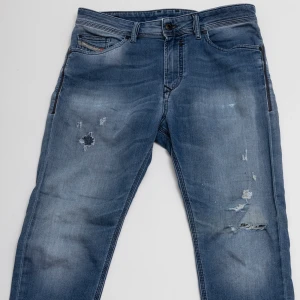 Diesel blå jeans med slitningar - Blå jeans från Diesel med snygga slitningar och lagade hål på framsidan. Klassisk femficksmodell, normal passform och raka ben. Jeansen har en tvättad look med ljusare partier och detaljerade sömmar på bakfickorna. Perfekt för dig som gillar en avslappnad stil.
