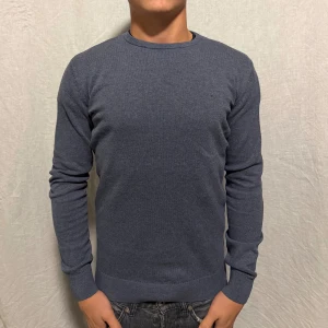 Blå Crew Neck från TomTailor - Säljer en stilren mörkblå crew neck tröja från TomTailor. Tröjan har rund halsringning, ribbade muddar och diskret logga på bröstet. Perfekt för dig som gillar en clean och klassisk look.