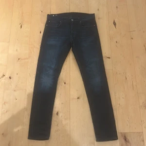Mörkblå jeans från G-Star RAW, 30/34 - Snygga svart/mörkblå jeans från G-Star RAW i storlek 30/34. Modellen har klassisk femficksdesign, slimmade ben och en snygg wash. Jeansen är tillverkade i ett denimtyg som sitter skönt och följer kroppen. Perfekt för dig som gillar stilrena och moderna jeans.
