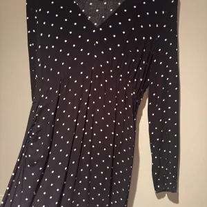 Svart lång prickig klänning H&M (MAMA) - Svart långklänning från H&M med vita prickar, v-ringad hals och långa ärmar. Klänningen har en lätt rynkad midja och är gjord i 100% Viscos som faller snyggt. Perfekt för dig som gillar klassiska mönster med en modern twist. Mama kollektion (Både under och efter graviditet) använd vid 1 tillfälle.