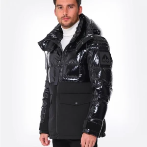 Svart pufferjacka från Moose Knuckles - Säljer en svart pufferjacka från Moose Knuckles med glansig yta upptill och matt tyg nedtill. Jackan har stor huva, dragkedja, flera fickor med lock och en snygg patch på ärmen. Perfekt för dig som vill ha en stilren och modern vinterjacka.