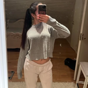 Grå croppad stickad tröja Divided - Grå croppad stickad tröja från Divided med rund hals och långa ärmar. Tröjan har ribbade muddar vid ärmslut och nederkant, samt en loose passform som ger en chill vibe. Perfekt för lager-på-lager under höst och vinter.