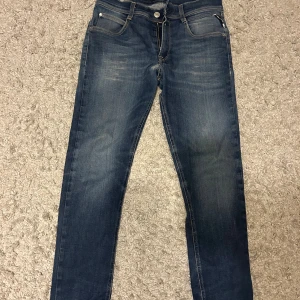  Replay jeans - Snygga mörkblå jeans från Replay med klassisk femficksdesign och diskreta slitningar. Jeansen har raka ben och normal passform, med Replay-logga på bakfickan och ljust märke i midjan. Perfekta till en avslappnad stil.