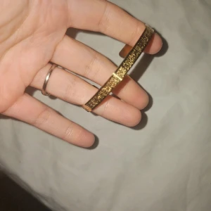 Guldigt armband med gravyr ayatul kursi - Snyggt armband i guldfärg med detaljerad gravyr längs hela ytan. Armbandet har en klassisk, smal form och är öppet i ena änden för enkel påtagning. Perfekt för dig som gillar unika accessoarer med lite extra karaktär.