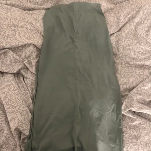 Grön långkjol i - Snygg grön långkjol med en lätt glansig finish. Kjolen har en rak passform och en enkel, stilren look som passar perfekt till sneakers eller boots. Den har en diskret omlott-detalj framtill som ger en extra touch.