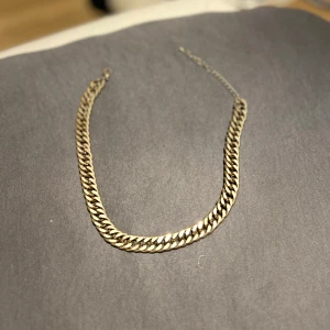 Kedjehalsband i guldfärg - Snyggt halsband med breda, platta länkar i guldton. Kedjan har en klassisk design som ger en cool och trendig look. Perfekt att bära som statement-piece till din outfit.