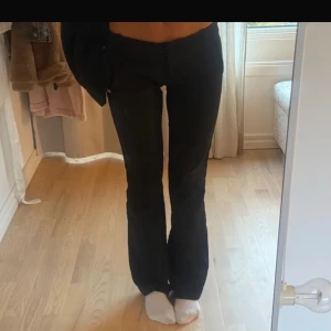 Svarta kostymbyxor Bik Bok Vera Tall - Svarta kostymbyxor från Bik Bok, modell Vera Tall. Byxorna har hög midja, raka ben med lätt bootcut och bälteshällor. Snygg och stilren passform som sitter tajt upptill och släpper vid benen. Perfekta för en clean och trendig look.