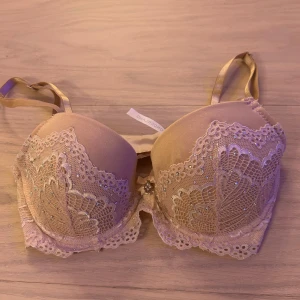 Beige korsett från Wonderland med spets - Säljer en rosa bh från Wonderland i storlek 70C. Bh har vacker spets med glittriga detaljer och en liten rosett med smycke mellan kuporna. Axelbanden är justerbara och materialet känns mjukt och lyxigt. Perfekt för dig som gillar eleganta underkläder.