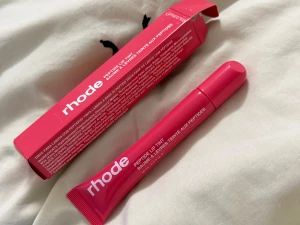 Rhode Peptide Lip Tint Guava Spritz - Rhode Peptide Lip Tint i färgen Guava Spritz. Ett läppbalsam med tint som ger en fräsch rosa nyans och återfuktar läpparna. Kommer i en smidig tub med vit text och snyggt rosa förpackning. Perfekt för dig som vill ha både färg och vård till läpparna.