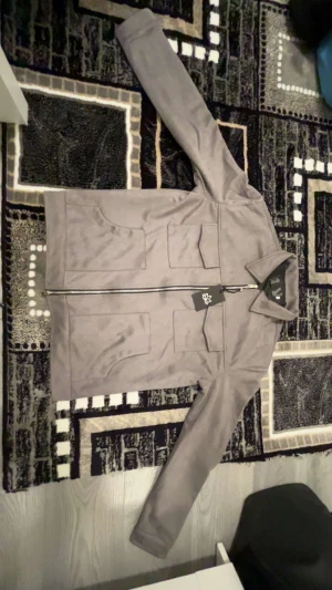 VELOUR JACKA  - Snygg grå overshirt i mocka-look med fyra stora fickor framtill och hel dragkedja. Den är oanvänd i storlek S. 