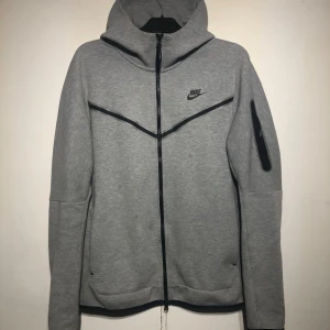 Nike Tech Grey Top - Nike Tech Fleece Hoodie – Grå (Storlek Medium) Säljer en snygg och bekväm Nike Tech Fleece hoodie i grå färg, storlek Medium. Använd sparsamt och är i mycket gott skick – inga fläckar, hål eller andra skador. Stilren design med svarta detaljer, dragkedja på ärmen och två praktiska framfickor med dragkedja. 🔹 Modell: Nike Tech Fleece 🔹 Storlek: Medium 🔹 Färg: Grå 🔹 Skick: Mycket bra, endast använd ett fåtal gånger 🔹 Nypris: ca 1 299 kr Perfekt för både träning och vardag! Pris kan diskuteras.