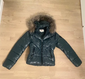 Mörkgrön pufferjacka från ONLY - Säljer en mörkgrön pufferjacka från ONLY med fluffig fuskpäls på huvan. Jackan har två fickor med dragkedja, quiltad design och lång ärm. Perfekt för kalla dagar och har en snygg, lite kortare passform. HELT NY OANVÄND💗💗💗 säljer för att jag inte vill ha en grön jacka!