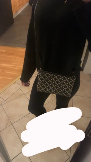 Svart axelväska från By Malene Birger - Snygg svart axelväska från By Malene Birger med beige grafiskt mönster och guldfärgad dragkedja. Väskan har en rektangulär form och justerbar axelrem. Materialet är skinn med textilfoder. Perfekt storlek för det viktigaste och stilren design.