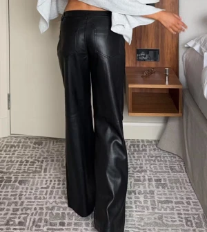 Skinn bootcut byxor - Snygga svarta byxor med bootcut och skinnimitation. Byxorna har klassiska bakfickor och en stilren look som passar perfekt till en trendig outfit. Materialet ger en cool vibe och byxorna sitter bekvämt över höfterna.