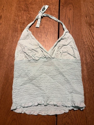 Ljusblå broderad linnetopp - Supersöt ljusblå linnetopp med knyt i nacken och broderade blommor upptill. Toppen har smockad midja och en liten volangkant längst ner. Perfekt för varma dagar och ger en chill vibe med sin ärmlösa design. 