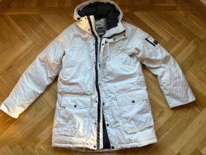 Vit jacka från Everest med huva - Säljer en vit jacka  från Everest i storlek 42. Jackan har en quiltad insida, stor huva, flera fickor med lock och dragkedja framtill. Perfekt för kalla dagar och har en clean look med svarta detaljer på insidan och ärmen.