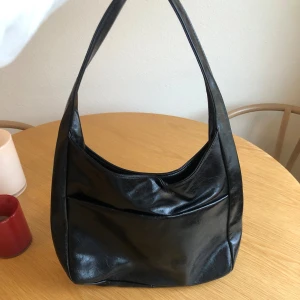 Svart väska  - Svart axelväska i faux läder. Väskan är rymlig och rymmer en 13-tums MacBook.  Modellen stängs med magnetknapp (ingen dragkedja) och har ett separat innerfack med dragkedja. På utsidan finns även ett ytterfack.   Köpt via TikTok Shop och endast sparsamt använd. Svag faux leather-doft kan förekomma