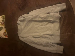 Grå sweatshirt från Stone Island - Säljer en clean grå sweatshirt från Stone Island med klassisk patch på vänster ärm. Tröjan har rund hals, långa ärmar och ribbade muddar. Perfekt för dig som gillar streetwear och vill ha något stilrent med ikonisk logga.